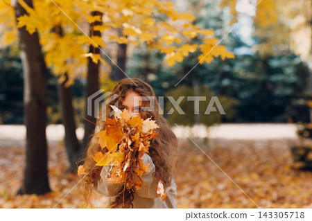 Smiling young woman collects leaves for the herbarium in the forest at sunset. Smiling young woman collects leaves for the herbarium in the forest at sunset. 143305718
