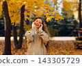 Smiling young woman with curly hairstyle enjoys the autumn weather in the forest with the yellow leaves at sunset. 143305729