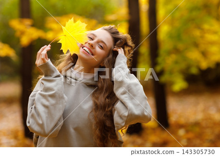 Young laughing woman holds yellow leaf in her hand in the park at sunset. 143305730