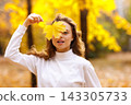 Young woman holds yellow leaf in her hand with smile in the park at sunset. 143305733