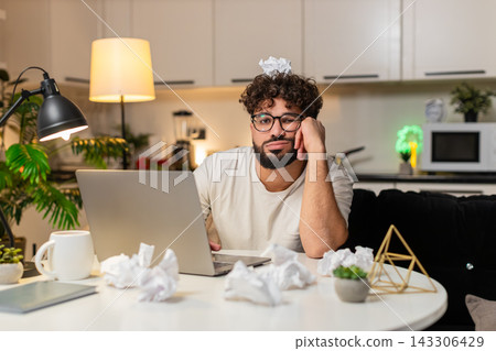 Arabian man frustrated with creative block sits with crumpled papers on desk writes ideas at night Arabian man frustrated with creative block sits with crumpled papers on desk writes ideas at night 143306429