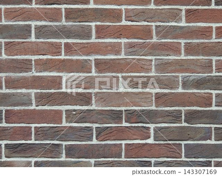 Rustic-style brick wall texture. Red and brown facing brick with a textured surface and gray cement mortar joints. Background for design, architecture, construction, and loft-style interiors. Rustic-style brick wall texture. Red and brown facing brick with a textured surface and gray cement mortar joints. Background for design, architecture, construction, and loft-style interiors. 143307169