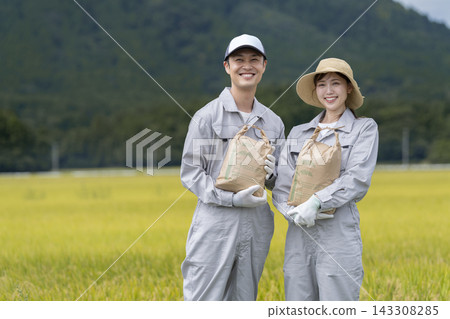 A rice farming couple, smiling and looking at the camera while holding a rice sack. A rice farming couple, smiling and looking at the camera while holding a rice sack. 143308285