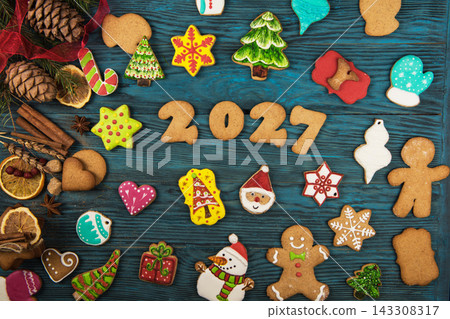 Christmas gingerbread cookies for New Year 2027 with snowman, Santa, and tree shapes on blue wooden background 143308317