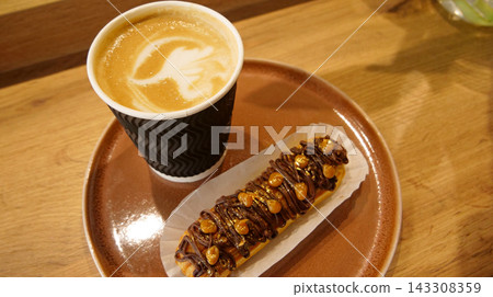 Pattern on a cappuccino foam in craft paper cup served with handmade french cake with nuts and chocolate icing at coffee shop Pattern on a cappuccino foam in craft paper cup served with handmade french cake with nuts and chocolate icing at coffee shop 143308359