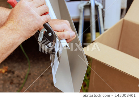 Contractor uses shears tool to cut gutter metal material near at workplace during assemble new gutters Contractor uses shears tool to cut gutter metal material near at workplace during assemble new gutters 143308401