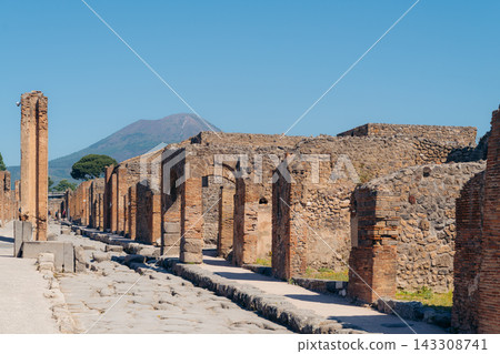Tourists walking through the archaeological ruins of Pompeii with Mount Vesuvius in the background Tourists walking through the archaeological ruins of Pompeii with Mount Vesuvius in the background 143308741