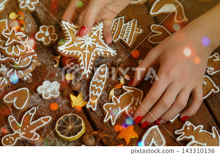 Woman decorates a festive christmas table with gingerbread cookies. Hands hold tasty cookies in form of heart or love shaped. Woman decorates a festive christmas table with gingerbread cookies. Hands hold tasty cookies in form of heart or love shaped. 143310136