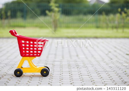 Bright plastic colorful shopping cart toy outdoors on sunny summer day. Bright plastic colorful shopping cart toy outdoors on sunny summer day. 143311120