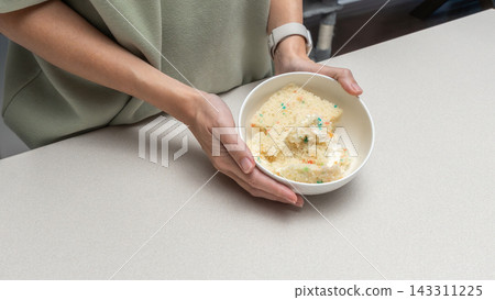 Woman mixing cake scraps with cream in bowl on kitchen table, homemade baking process, dessert preparation stage, cozy home cooking lifestyle. Woman mixing cake scraps with cream in bowl on kitchen table, homemade baking process, dessert preparation stage, cozy home cooking lifestyle. 143311225