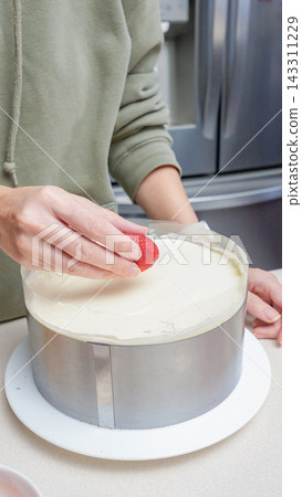 Person decorating a round cake with fresh strawberries in a modern kitchen, stainless steel appliances visible in the background Person decorating a round cake with fresh strawberries in a modern kitchen, stainless steel appliances visible in the background 143311229