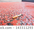 Discarded cigarette butt on red pavement 143311293