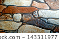 High-quality background of a rustic stone wall texture featuring irregular, interlocking rocks in earth tone shades of brown, terracotta, beige, and gray. The structured surface showcases detailed mas 143311977
