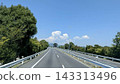 A winding highway under a summer sky, surrounded by greenery. 143313496