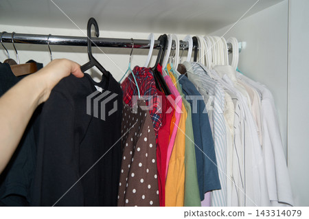 Hand Pulls Black Shirt Forward On Hanger From Colorful Row Inside Open Wardrobe, With Plaid Hand Pulls Black Shirt Forward On Hanger From Colorful Row Inside Open Wardrobe, With Plaid 143314079