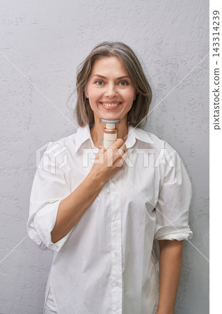 Smiling Woman Holding Handheld Neck Massage Device Against Gray Studio Wall In Casual Wellness Smiling Woman Holding Handheld Neck Massage Device Against Gray Studio Wall In Casual Wellness 143314239
