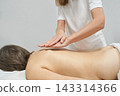 Female Massage Therapist Gliding Hands Across Client Back In Bright Treatment Room With White 143314366
