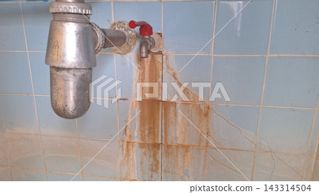 An old metal faucet leaks and leaves rust stains across the blue tiled wall An old metal faucet leaks and leaves rust stains across the blue tiled wall 143314504
