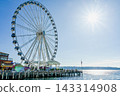 A giant Ferris wheel with dazzling sunlight and ocean views at 57 Pier in Seattle, USA. 143314908