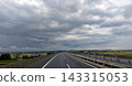 A highway under a cloudy sky with rain clouds spreading across it, and a rural landscape. 143315053