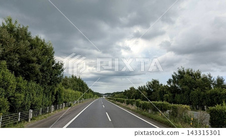 一條綠樹環繞的高速公路在厚厚的雲層下筆直向前延伸。 143315301
