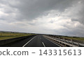 A highway curves through a rural area under a cloudy sky. 143315613