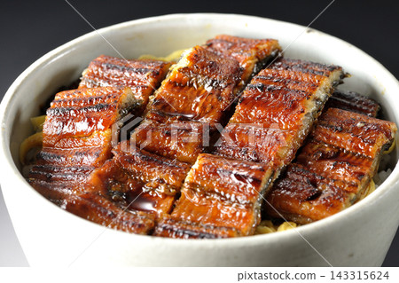 A single serving of eel rice bowl photographed against a black background. A single serving of eel rice bowl photographed against a black background. 143315624