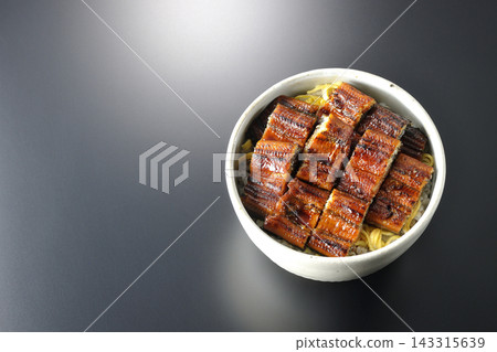 A single serving of eel rice bowl photographed against a black background. A single serving of eel rice bowl photographed against a black background. 143315639