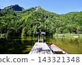 A clear, sunny day in Kamikochi, with the pier and torii gate at Myojin Pond, a boat, and the majestic Mt. Myojin standing in the background. 143321348