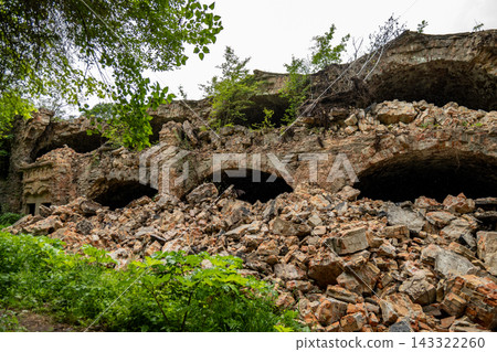 Old stone walls are in disrepair, with piles of rocks and rubble scattered around. Plants grow over parts of the ruins Old stone walls are in disrepair, with piles of rocks and rubble scattered around. Plants grow over parts of the ruins 143322260