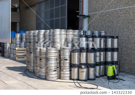 Many stainless steel beer kegs are stacked outside a brewery building, reflecting the industrial process of beer production and storage for distribution Many stainless steel beer kegs are stacked outside a brewery building, reflecting the industrial process of beer production and storage for distribution 143322330