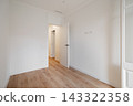Empty room with white walls and wooden floor. A door is slightly open, leading to another space. Natural light illuminates the area. 143322358