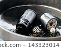 Used oil filter and drain plug sitting in an oil drain pan after an oil change 143323014