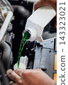 Mechanic pouring green coolant liquid into car engine 143323021