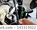 Mechanic pouring green coolant liquid into car engine 143323022