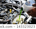Mechanic pouring green coolant liquid into car engine 143323023