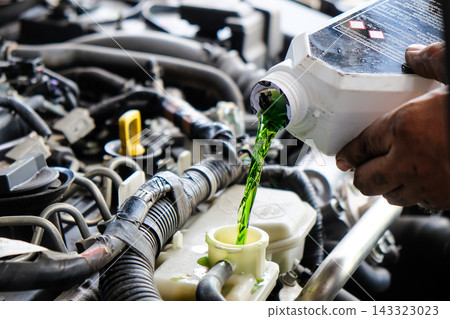 Mechanic pouring green coolant liquid into car engine Mechanic pouring green coolant liquid into car engine 143323023