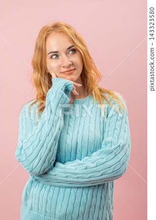 Young woman with red hair and blue eyes, wearing a cable knit sweater, looking up and resting her chin on her hand, contemplating, considering options, and concentrating on a decision Young woman with red hair and blue eyes, wearing a cable knit sweater, looking up and resting her chin on her hand, contemplating, considering options, and concentrating on a decision 143323580