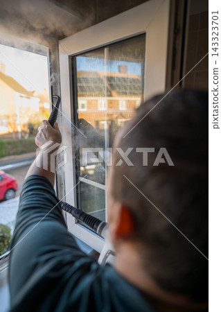 Cleaning the window. A man with steam device removes dirt from the plastic window frame. Cleaning the window. A man with steam device removes dirt from the plastic window frame. 143323701