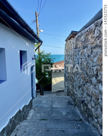 Narrow stone alley in Yalta descends toward bright blue Black Sea. 143323755
