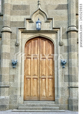 Ornate wooden double door sits within carved Gothic Revival stone entrance. Ornate wooden double door sits within carved Gothic Revival stone entrance. 143323933