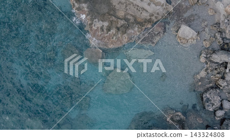 Top down aerial view of transparent blue ocean water with large submerged rocks and stones near wild coast reef seabed texture background for travel Top down aerial view of transparent blue ocean water with large submerged rocks and stones near wild coast reef seabed texture background for travel 143324808