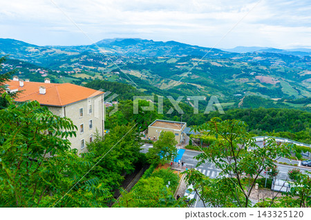 Republic of San Marino top view on the tiled roofs of the old town. Architecture and nature. Mountains fields and green agricultural lane. Republic of San Marino top view on the tiled roofs of the old town. Architecture and nature. Mountains fields and green agricultural lane. 143325120