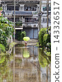 Person holding bright green umbrella wades through flooded residential street reflecting buildings and trees 143326517