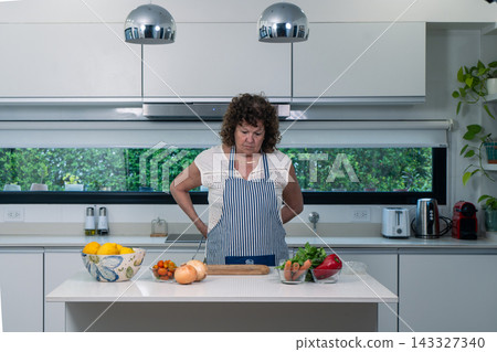 Older Focused cook pausing at her kitchen island amid gathered ingredients Older Focused cook pausing at her kitchen island amid gathered ingredients 143327340
