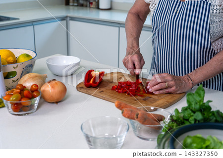 Hands skillfully chopping red peppers on a wooden board in a bright kitchen 143327350