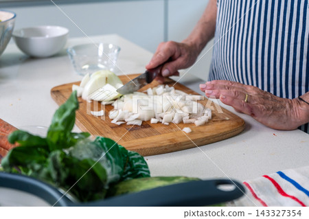 Senior preparing diced onions with steady precision at a modern kitchen counter Senior preparing diced onions with steady precision at a modern kitchen counter 143327354