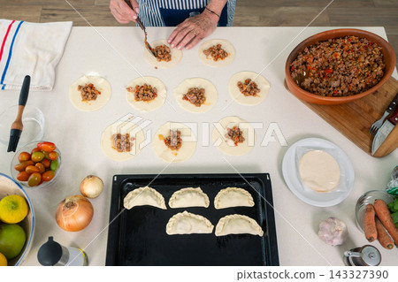 Distributing seasoned meat filling across fresh empanada rounds with practiced precision Distributing seasoned meat filling across fresh empanada rounds with practiced precision 143327390