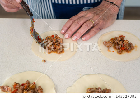 Spooning seasoned ground meat filling onto empanada dough circles with deliberate care Spooning seasoned ground meat filling onto empanada dough circles with deliberate care 143327392