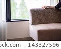 A woman's hand rests on the backrest of a couch. A bright room by the window. 143327596